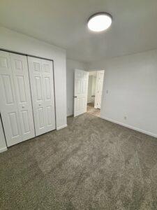 Empty bedroom with gray carpet, white walls, and double closet doors.