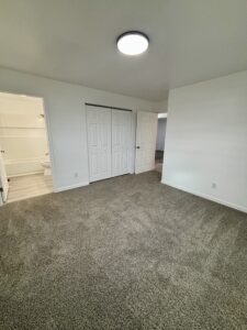Carpeted bedroom with white walls, ceiling light, and closet doors.